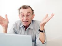 Ædre mand slår armene ud foran sin computer Foto: Colourbox