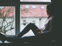 Silhouet af unge kvinde, der sidder i vindueskarm og ser ud