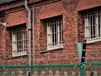 Fængsel med overvågningskamera set udefra over mur med pigtråd
