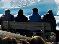 Fire mænd sidder på en bænk i Grønland og kigger på et ishav