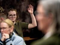 Ung kvinde rækker hånden op til borgermøde