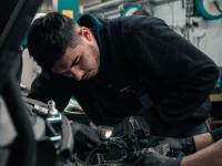 En ung mekaniker med minoritetsetnisk baggrund, der arbejder på en bil.