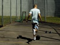 ryggen af ung dreng, der spiller fodbold på indhegnet bane bag høje mure